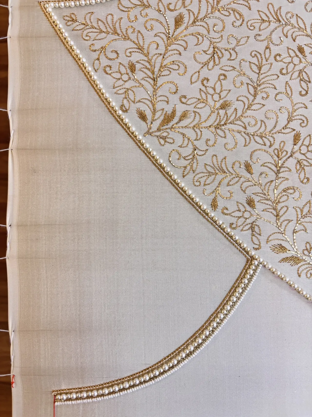 Ivory fabric on an embroidery frame with a gold-worked neckline and floral pattern.