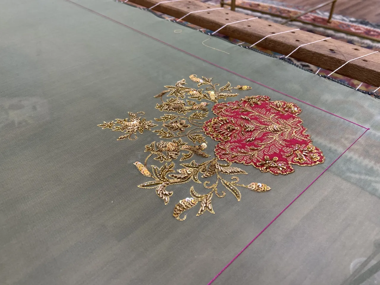 Gold and pink floral motif being embroidered on sheer fabric on a frame.