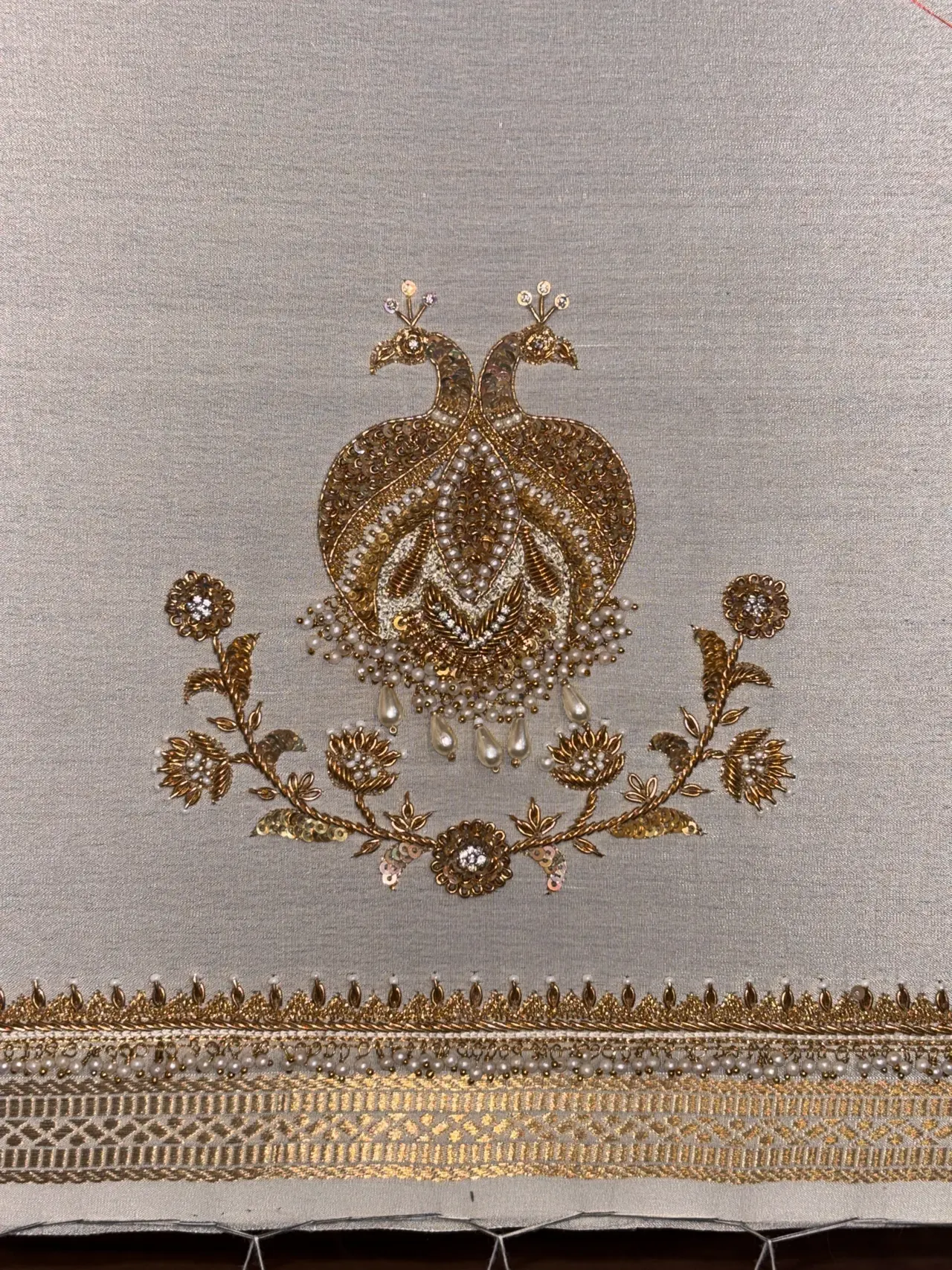 Gold embroidered twin-peacock motif on pale fabric with a woven border.