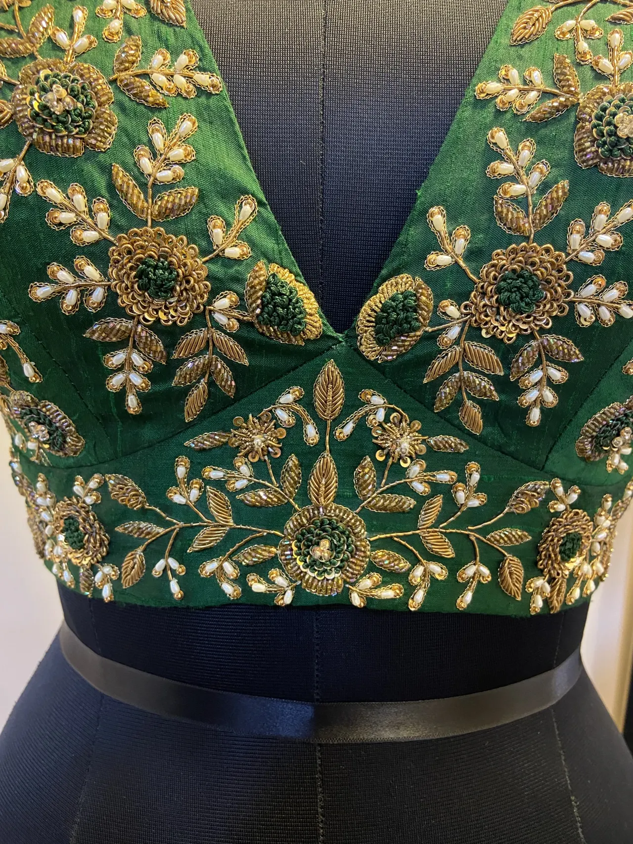 Close view of gold and green floral handwork across the neckline of a green blouse.