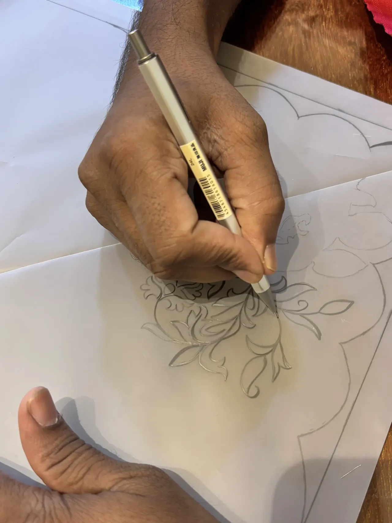 A hand drawing a floral motif in pencil on paper.