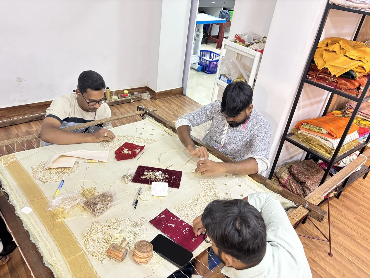 Artisans working at a large embroidery frame in the workroom.