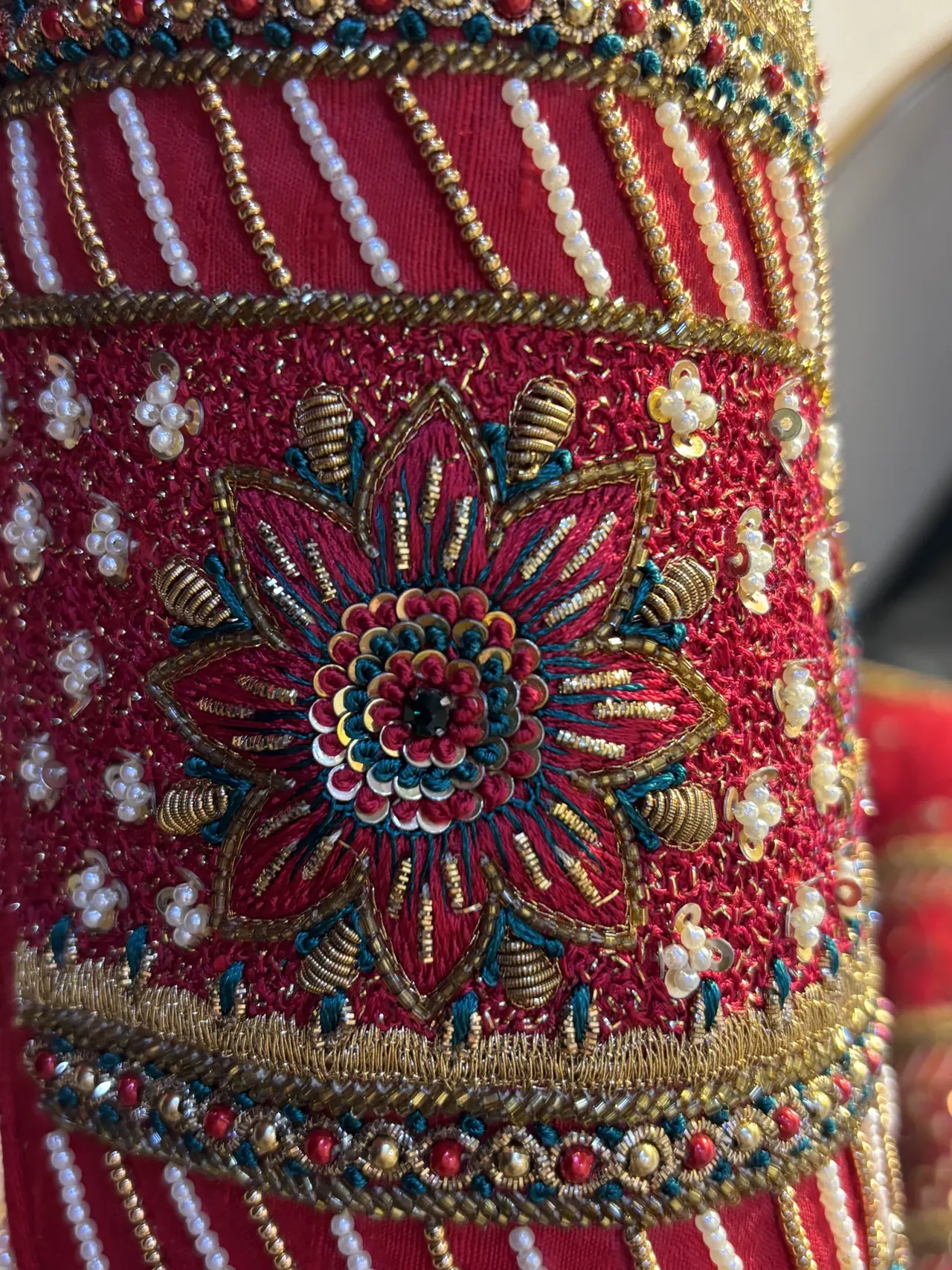Close view of a red sleeve with beaded floral embroidery and striped detailing.