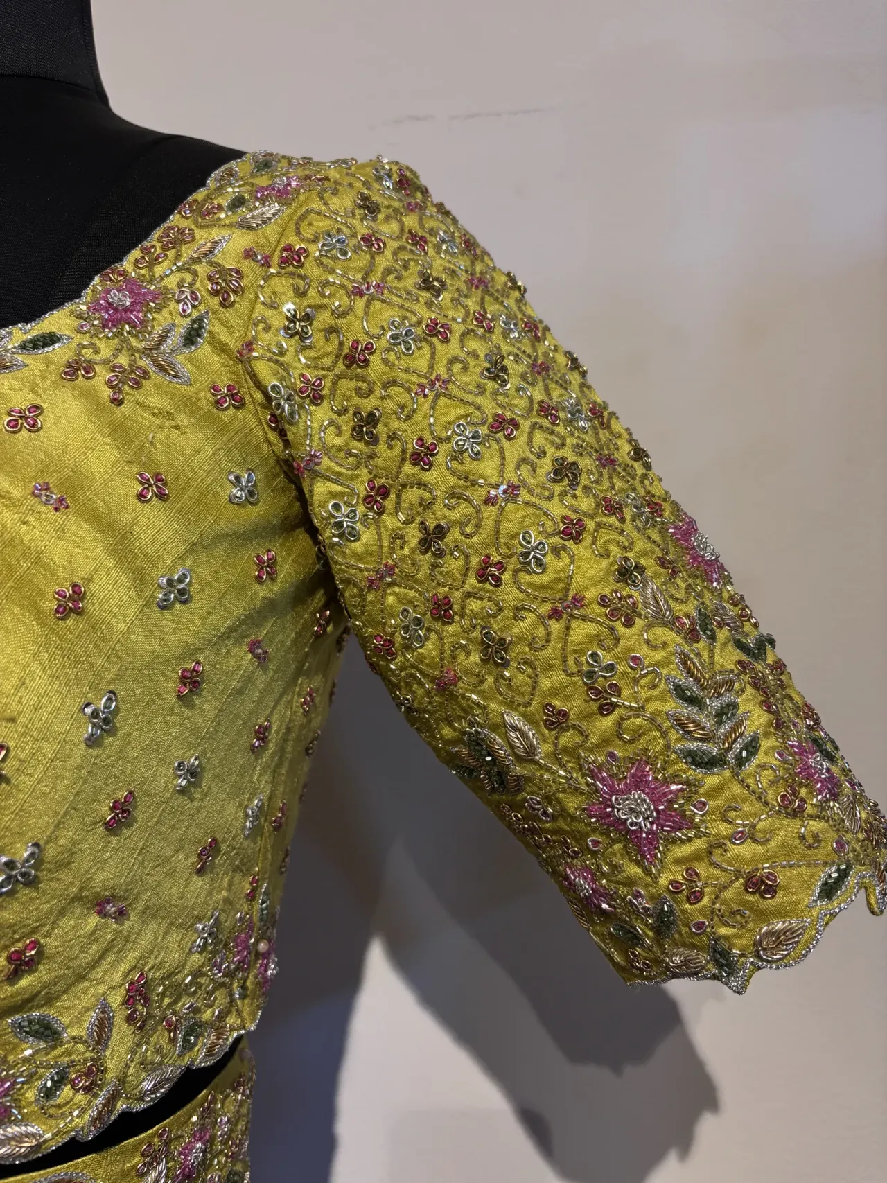Yellow blouse with fine floral embroidery on a dress form.